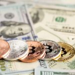 На зображені різні типи валют. Долари США та сверху монети зі значком біткоїна